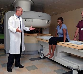 a patient sitting on an open mri machine talking to the radiologist